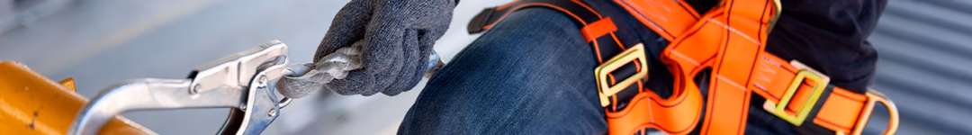 close up image of a construction worker clipping onto a railing using a harness for safety